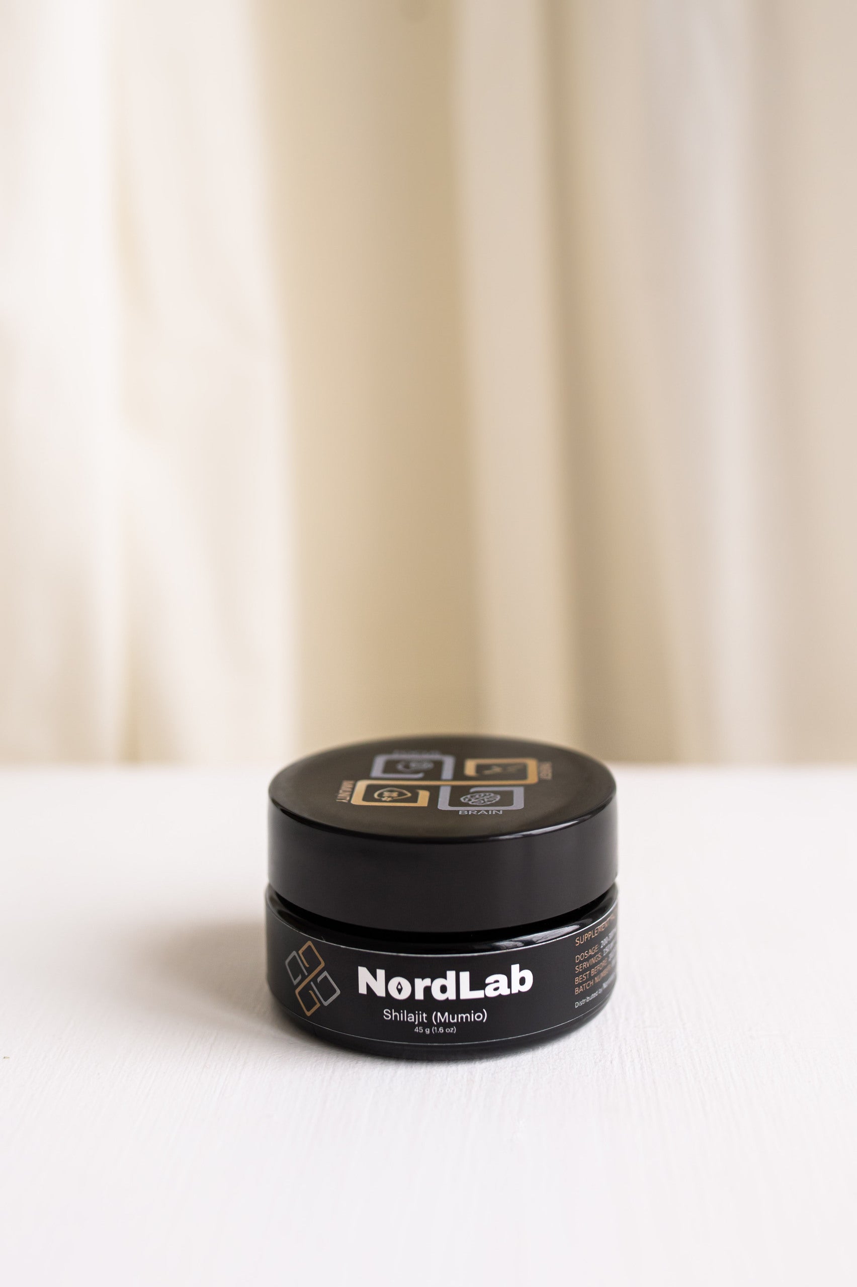 Black NordLab jar on a white surface with a beige curtain background