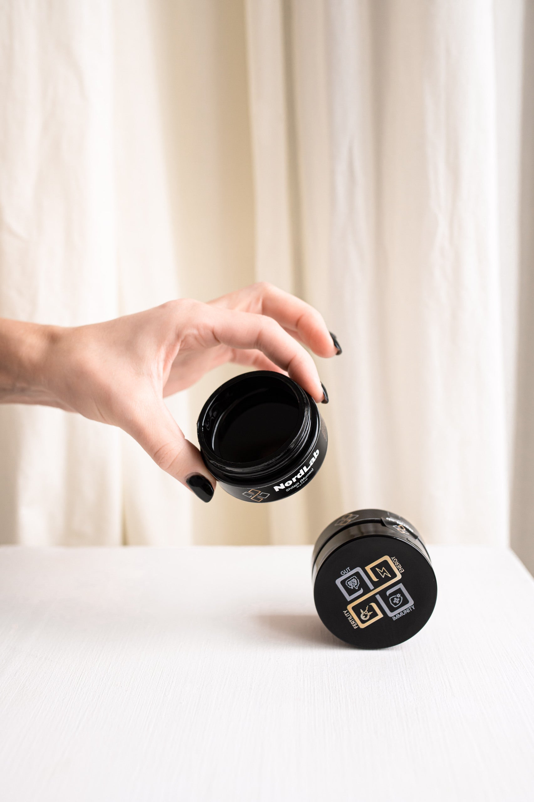 Hand holding a black travel mug with a visible brand logo against a white curtain background