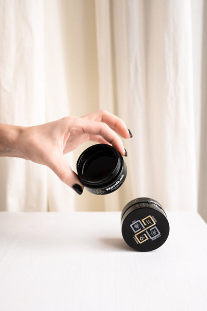 Hand holding a black travel mug with a visible brand logo against a white curtain background